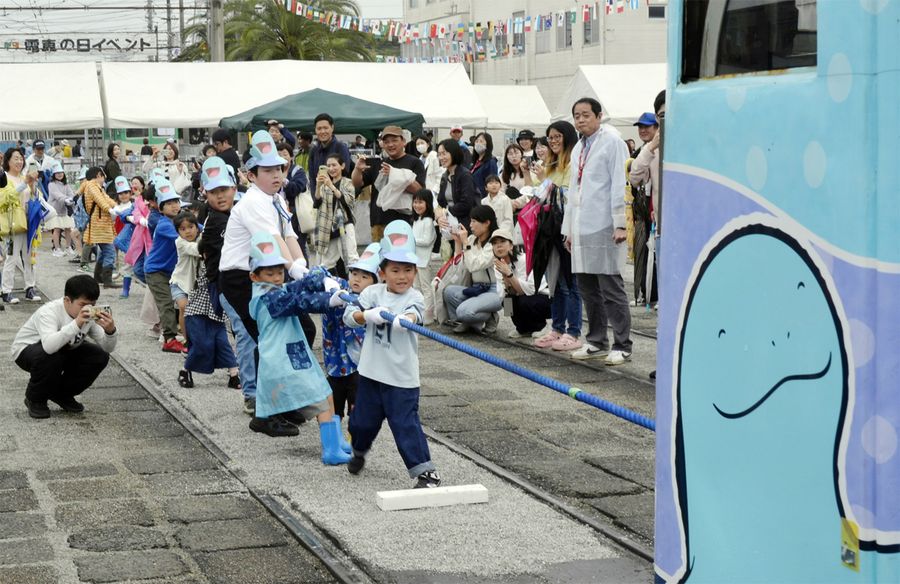 「ヌオー」ラッピング電車と綱引きをする子どもたち（高知市桟橋通４丁目）