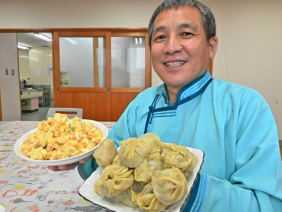 モンゴルの伝統衣装を着て、ブーズと首都サラダを手にするバスカさん（いずれも南国市の三和防災コミュニティーセンター）