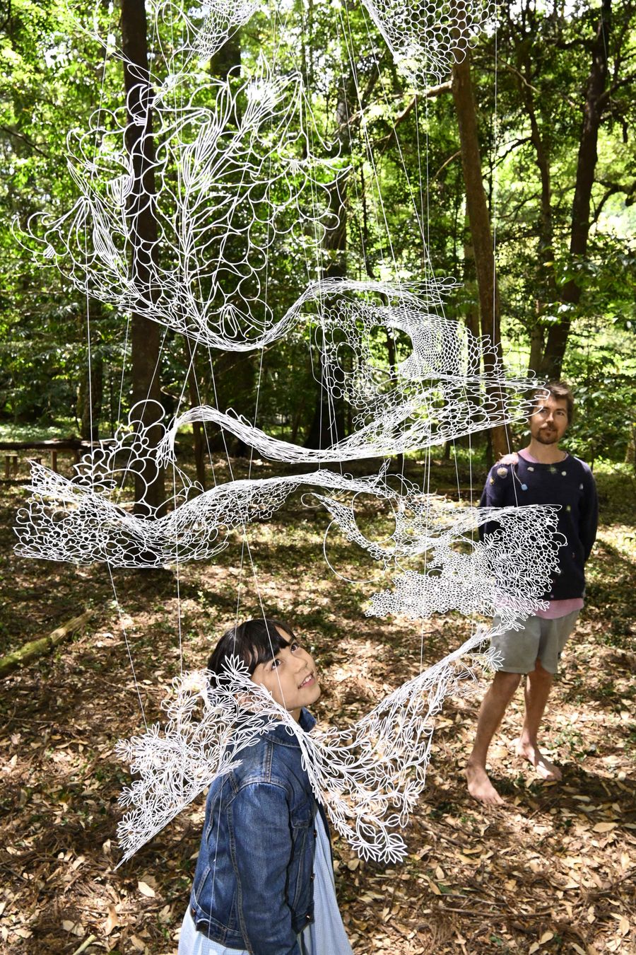 木漏れ日を受けた切り絵作品を楽しむ来場者たち（四万十町大正の熊野神社）