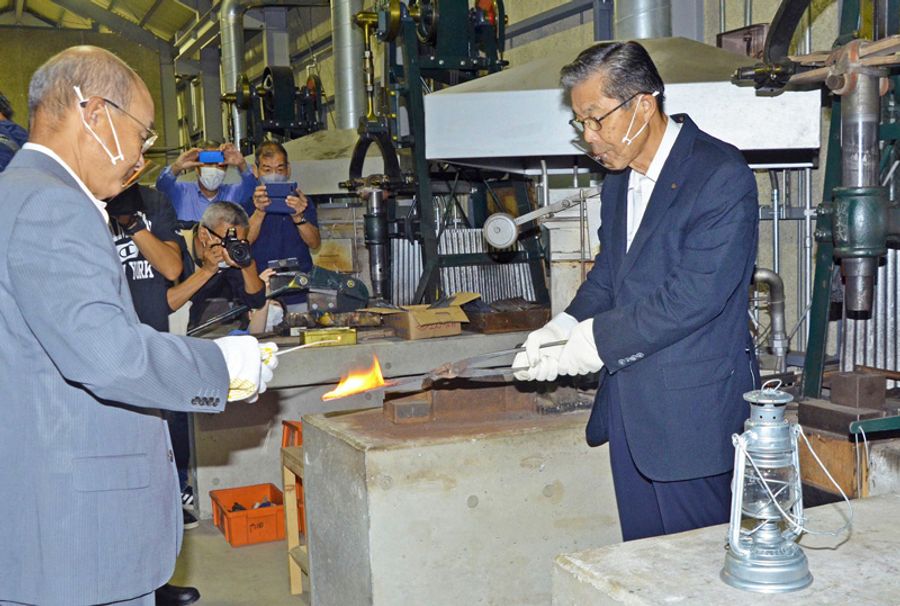 熱した鉈から採火する法光院晶一市長=左=と西山武塾長(香美市の鍛冶屋創生塾)