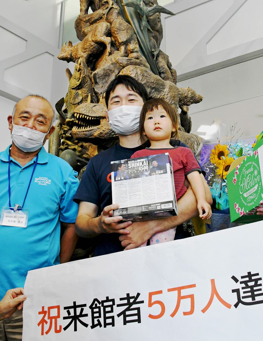 5万人目の入館者となり、記念品を受け取った溝渕拓也さん(中央)と美緒ちゃん(右)=南国市の海洋堂SpaceFactoryなんこく
