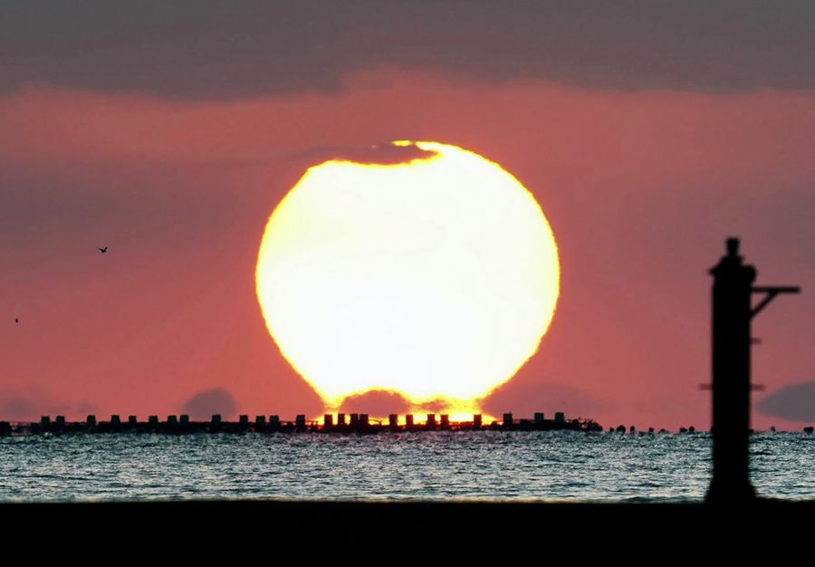 だるま夕日シーズン到来。養殖いかだの上、蜃気楼によって雲のように見えるのは九州の島（宿毛市小筑紫町小浦）