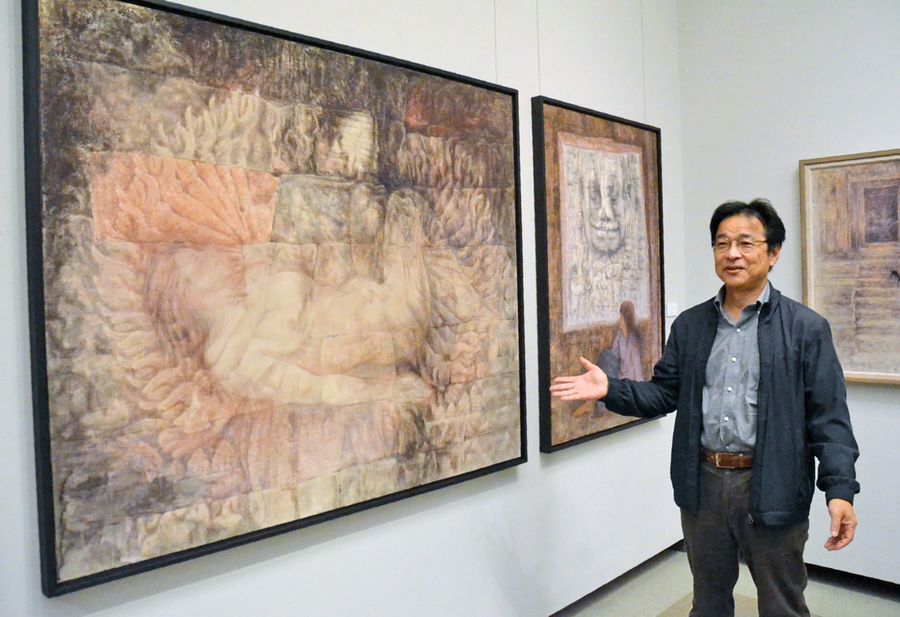 千手観音に抱かれる女性を描いた最新作の前に立つ市川雅彦。カンボジアの旅で着想を得た(香美市土佐山田町の香美市立美術館)