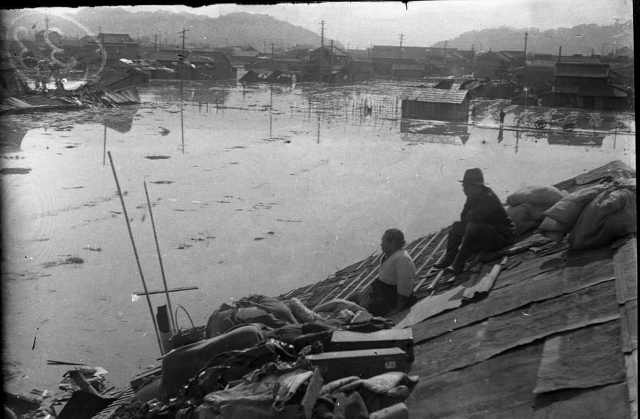 屋根の上に座り、浸水した町をぼうぜんと眺める住民(高知市の下知地区)