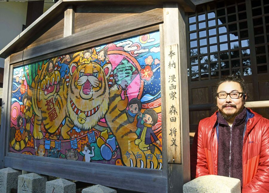 森田将文さん(右)が描いた絵馬。華やかな一作に仕上がった=香美市土佐山田町北本町2丁目の八王子宮