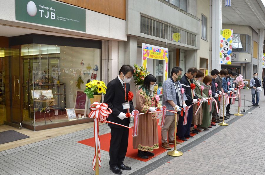 記念セレモニーでテープカットする出店経験者ら