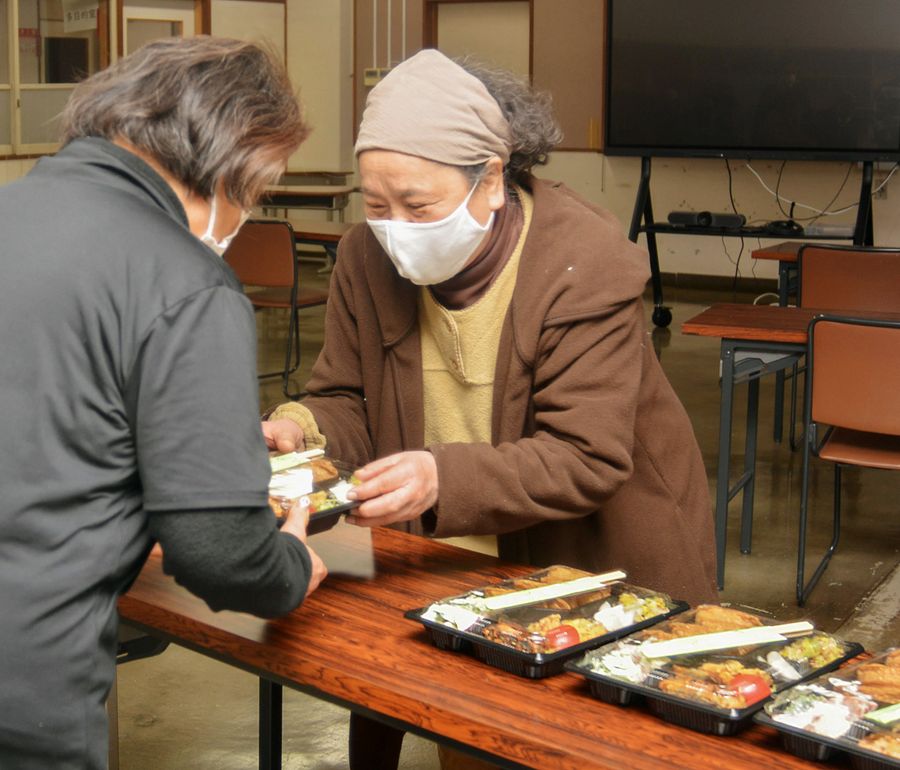 ボリュームたっぷりのお弁当を生徒に手渡す竹内喜美恵さん＝右（高知市の高知国際中学校夜間学級）
