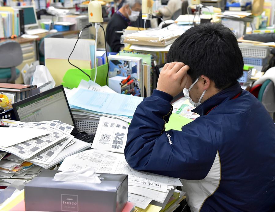 資料に囲まれて仕事をする教員。日常業務に加え、部活動の負担感も増している（県内の中学校）