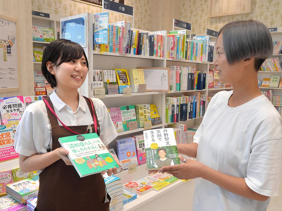 認知症フェアで構えた棚を背に談笑する小笠原杏樹さん=左=と認知症当事者の山中しのぶさん(高知市の未来屋書店高知店)