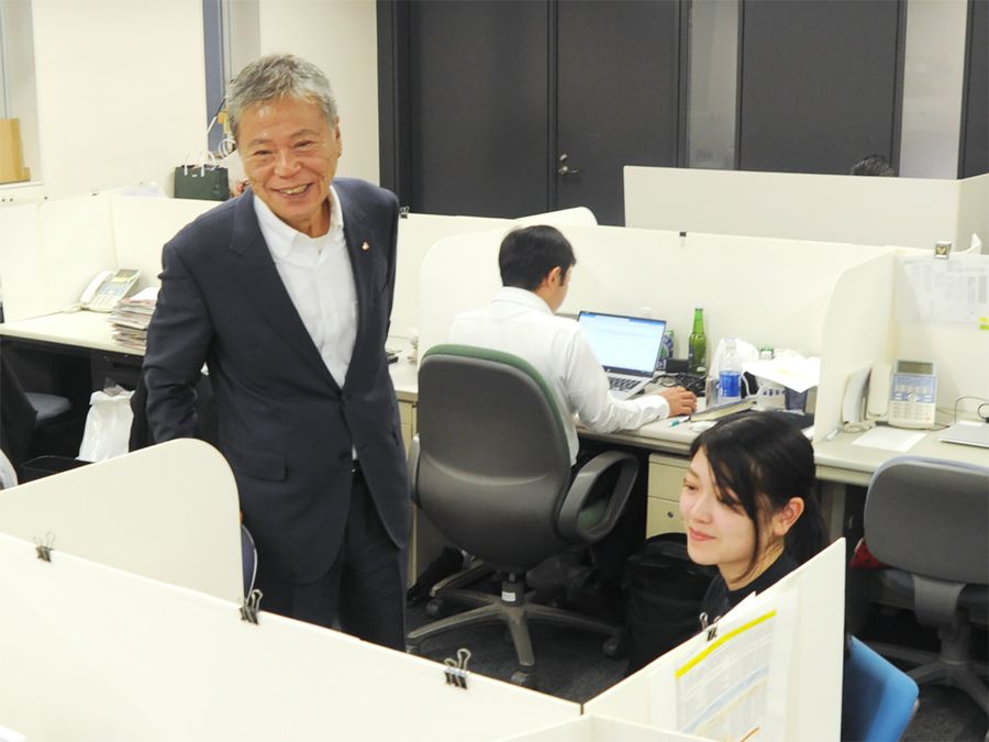 社員と談笑する相談役の竹内成雄。1990年の赴任から東京暮らしが続く（東京都港区の東京本部）