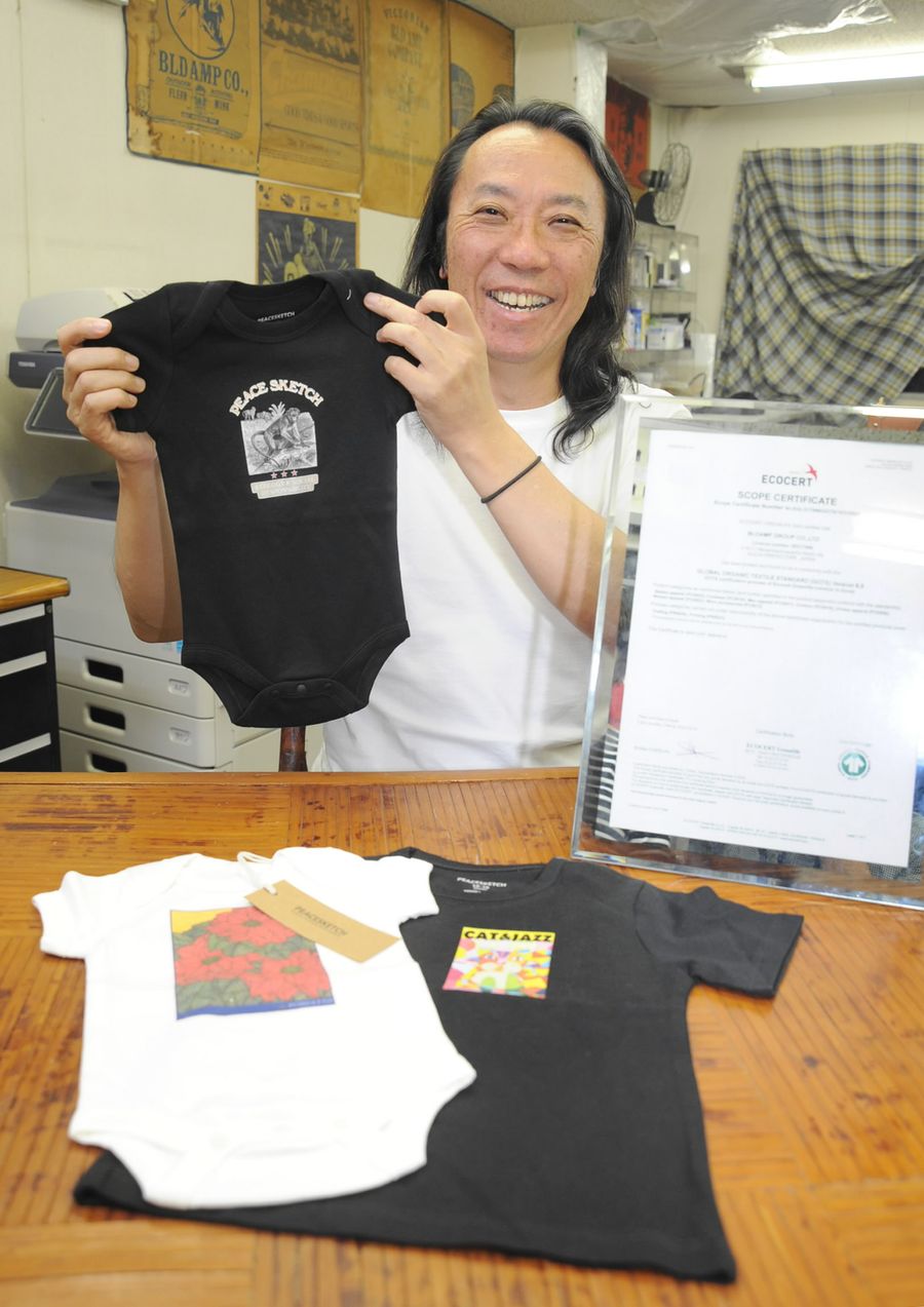 オーガニックコットンの赤ちゃん服を手にする北村英彦社長（高知市南はりまや町１丁目）