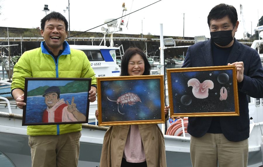 松尾拓哉さん（左）に深海生物を描いた絵をプレゼントした竹村広美さん（中央）＝室戸市の佐喜浜港