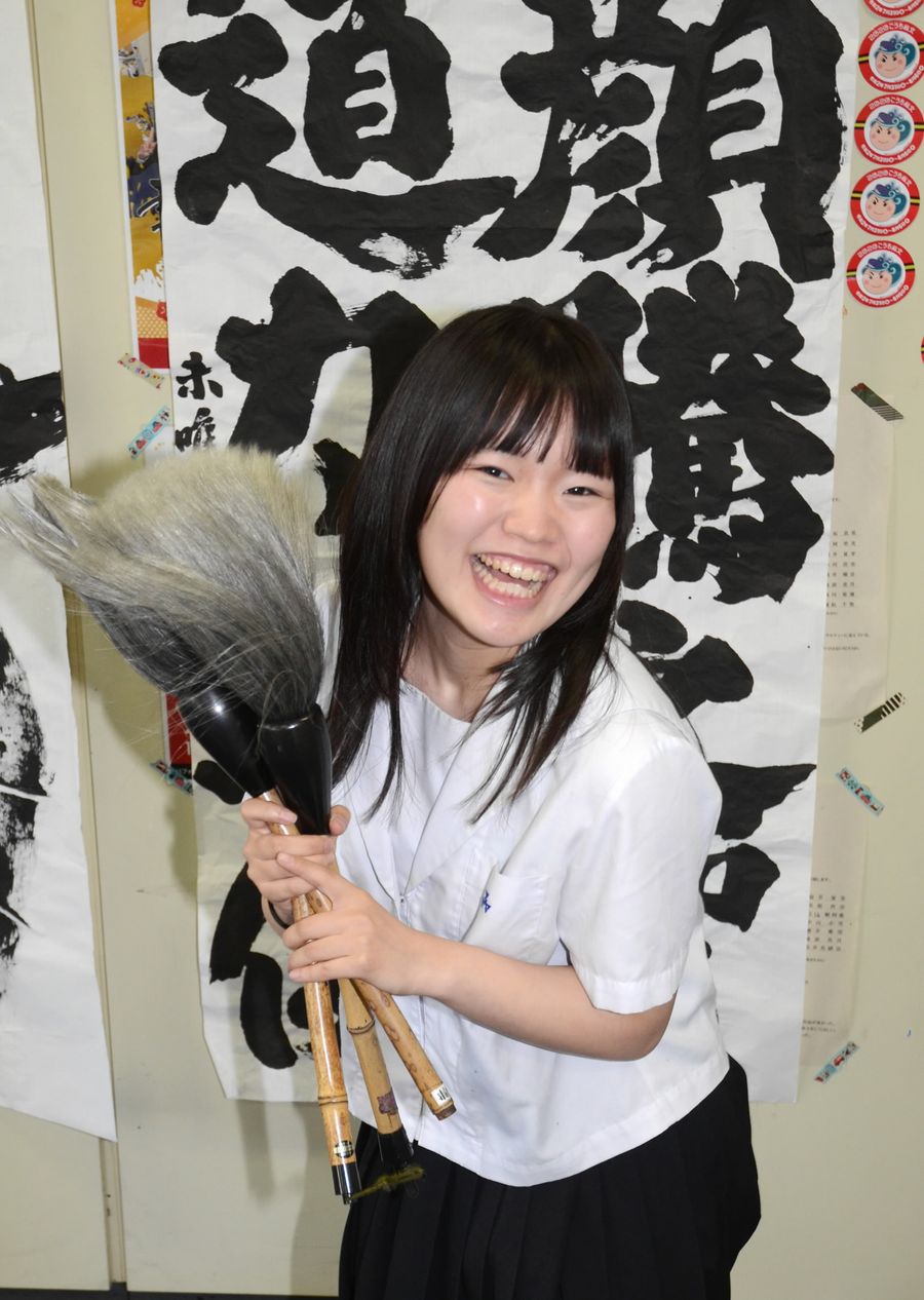 受賞作を書いた大きな筆を手に喜ぶ池沢未唯さん（高知市城北町の小津高）