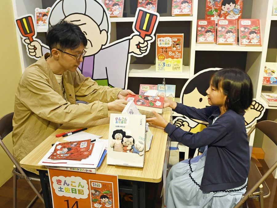 村岡マサヒロさんがファン一人一人に直筆のサイン本を手渡した（高知市の金高堂書店本店）