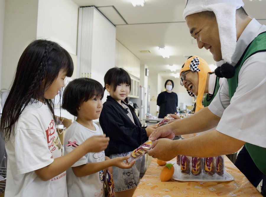 子ども食堂を訪れた児童らにお菓子を配るダイナムの社員(香南市の赤岡保健センター)