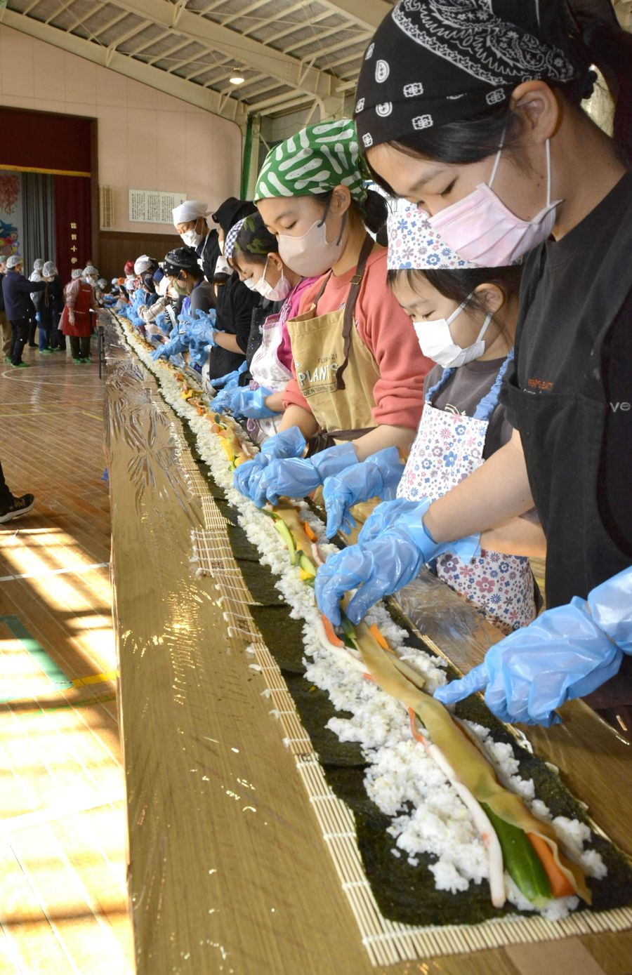体育館をいっぱいに使って全長２３メートル超の巻きずしを作った児童ら（黒潮町の佐賀小学校）