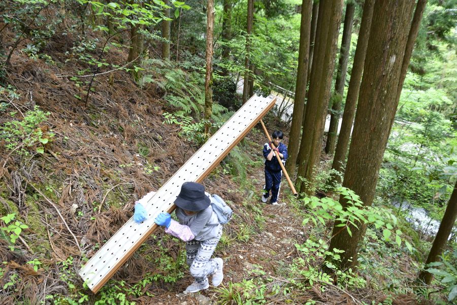 重い資材を担いで急斜面を登る地元有志