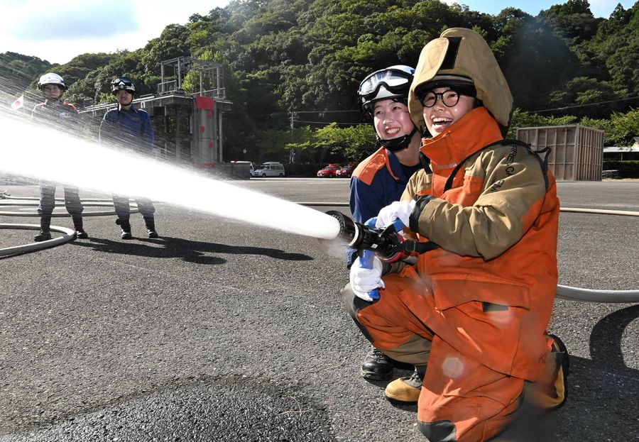 現役の女性消防士に支えられながら放水を体験したツアー参加者（いの町の県消防学校）