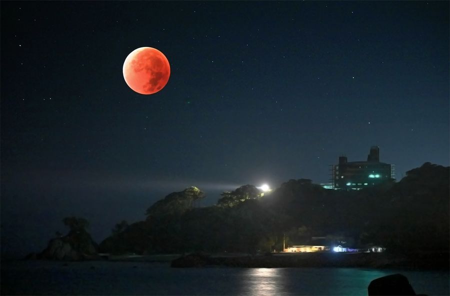 赤銅色に輝く満月と桂浜(8日午前3時35分、高知市浦戸から多重露光で撮影)