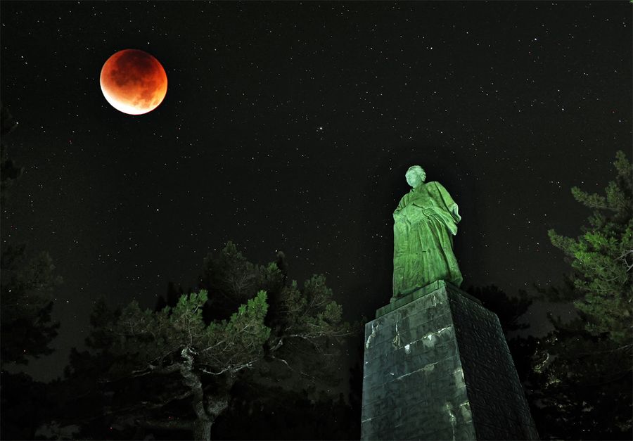赤銅に染まった月と坂本龍馬像(午前2時40分ごろ、多重露光で森本敦士撮影)