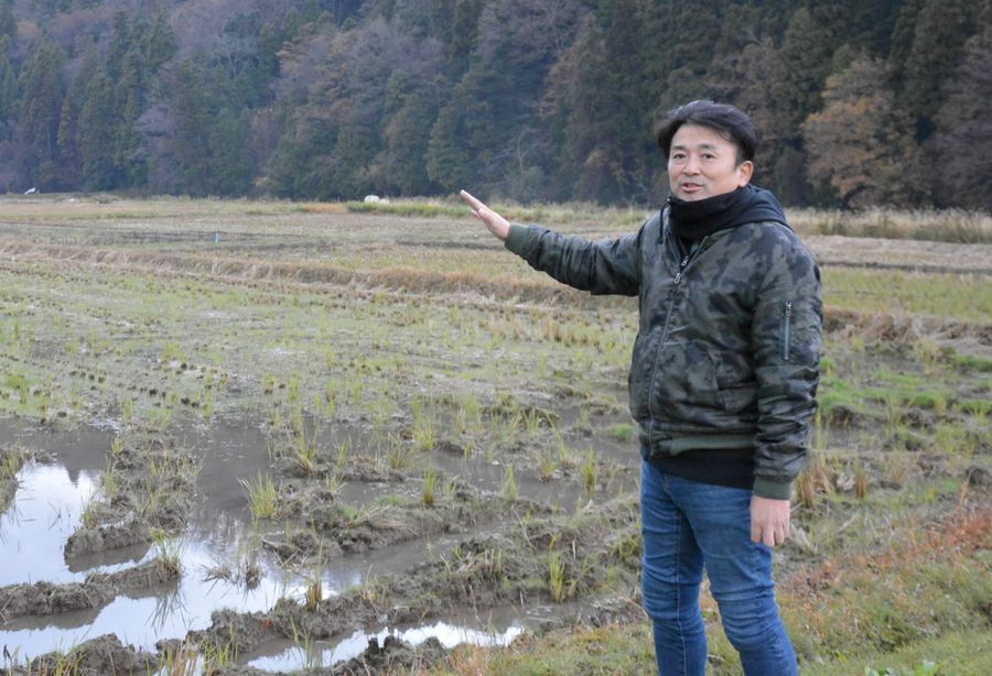 稲刈りを終えた水田の前で震災を振り返る川原伸章さん。近くの水路は曲がったままだ（石川県珠洲市町野町）