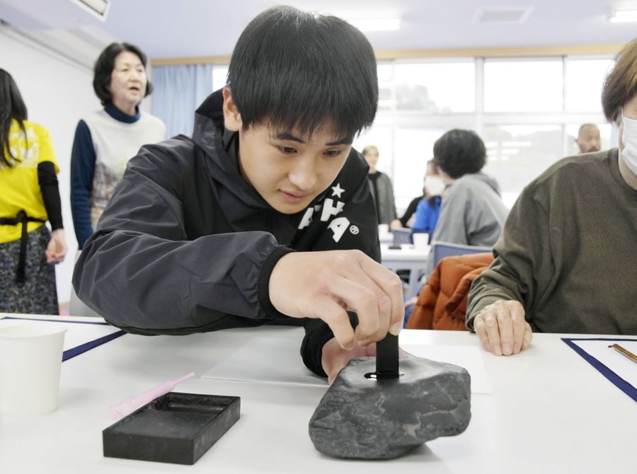 元海岸の石で作った硯で書道体験する参加者（22日、室戸市室戸岬町の室戸世界ジオパークセンター）