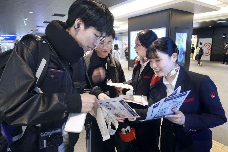 モバイルバッテリーの利用について乗客にチラシを配る航空会社の関係者＝４月１４日、羽田空港